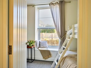 A bedroom with a window, a bedside table with a plant, a bunk bed, and a curtain. - Elegant Riverside Apartment for 4 (Bude)