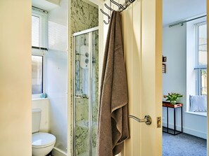 A bathroom with a glass-enclosed shower, a toilet, and a towel hanging on a door handle. - Elegant Riverside Apartment for 4 (Bude)