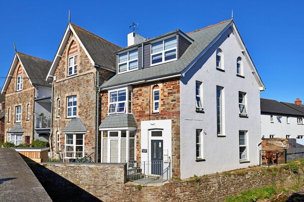 A row of stone and plaster houses with a central door and windows, a stone wall, and a paved path. - Elegant Riverside Apartment for 4 (Bude)