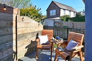 A wooden deck with two wooden chairs and a small table, a house in the background, and a wooden fence. - Elegant Riverside Apartment for 4 (Bude)