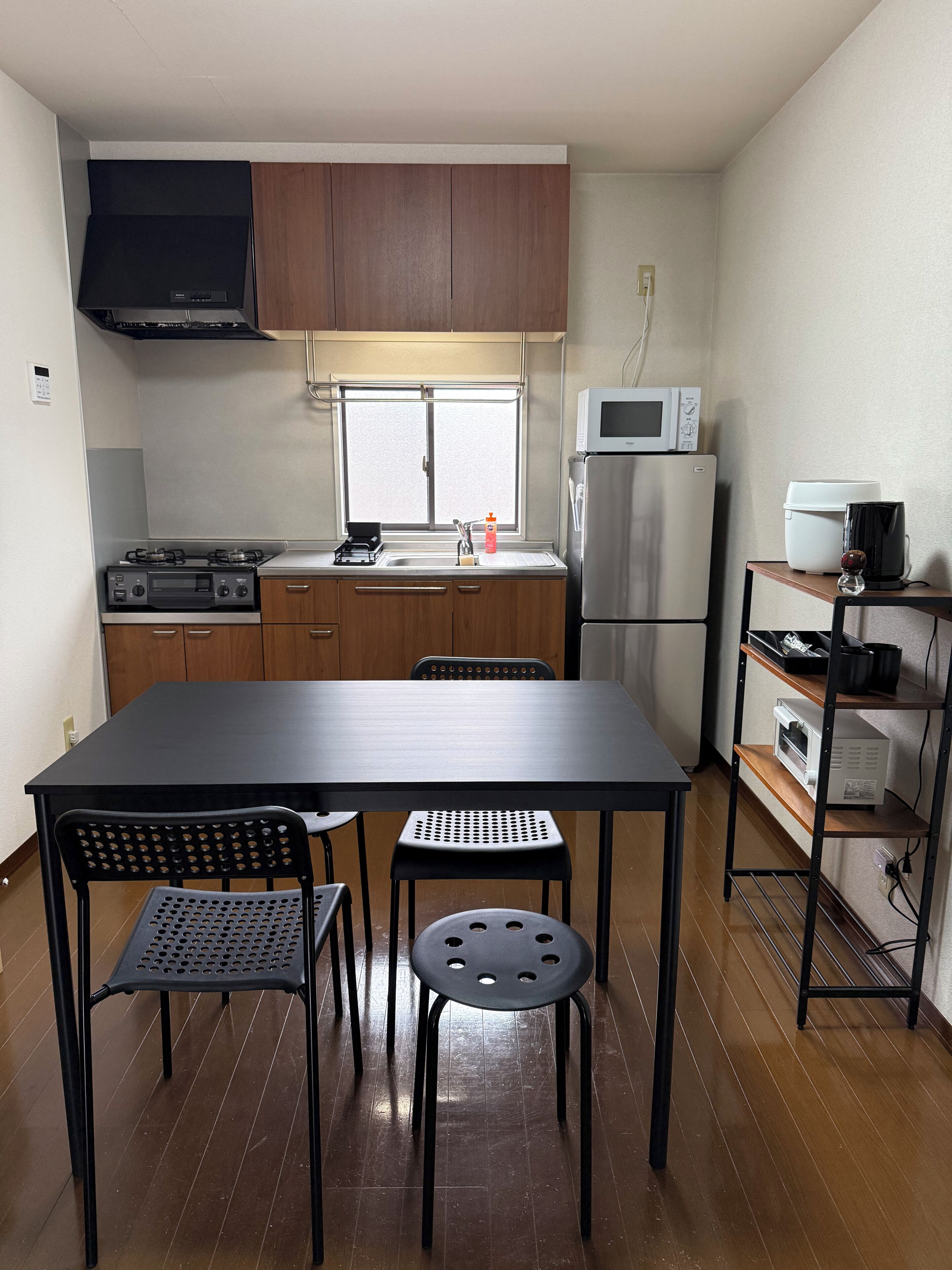 A compact kitchen with a dining table, chairs, a microwave, a refrigerator, and a coffee machine.