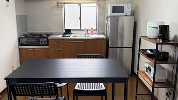 A compact kitchen with a dining table, chairs, a microwave, a refrigerator, and a coffee machine.