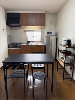 A compact kitchen with a dining table, chairs, a microwave, a refrigerator, and a coffee machine.