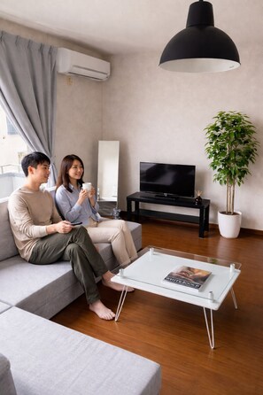 A modern living room with a sofa, a coffee table, a TV, and a potted plant. - [Newly Opened!!] Conveniently located just 3 stops and 9 minutes from Okayama Station! Up to 6 people! Free parking! With a kitchen and cooking utensils, it's perfect for long-term stays! Separate Bath and Toilet! There's even a big park! (岡山市中区兼基)