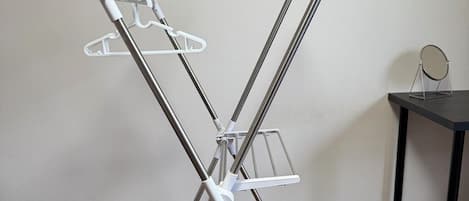 A metal drying rack with multiple hangers and a small round mirror on a table.