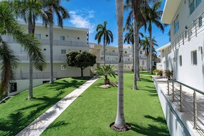 A courtyard with palm trees, a neatly trimmed lawn, and a building with balconies.