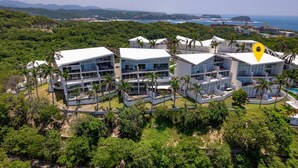 Un hotel moderno con varias edificaciones blancas, rodeado de exuberante vegetación y vistas al mar.