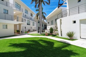 A modern multi-story residential building with balconies, a central courtyard with artificial grass, and potted plants.