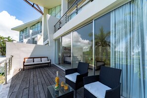 A modern outdoor balcony with a sofa, wicker chairs, and a table with a bottle and glasses.