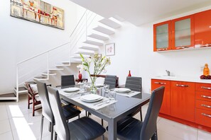 Ein moderner Essbereich mit einem Glastisch, schwarzen Stühlen, einer weißen Treppe und roten Schränken.