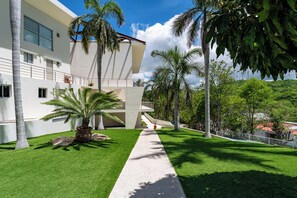 A modern building with a white facade, a central staircase, and a well-maintained lawn with palm trees.