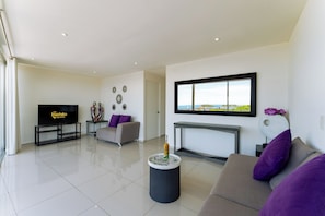 A modern living room with a flat-screen TV, a sofa, a coffee table, and a fireplace. - Main Level 2BR | Oceanview, Pool & Beach (Huatulco)