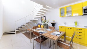 A modern kitchen with yellow cabinets, a stainless steel oven, and a dining area with a wooden table and chairs. - Main Level 2-Story 2BR | Pool, Gym & Beach (Huatulco)