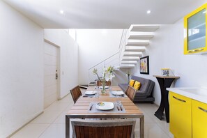 A compact living space with a dining area, a sofa, a staircase, and a kitchen area. - Main Level 2-Story 2BR | Pool, Gym & Beach (Huatulco)