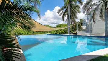 A clear blue swimming pool with a rope barrier, surrounded by palm trees and a building with a white facade.