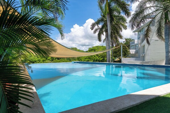 A clear blue swimming pool with a rope barrier, surrounded by palm trees and a building with a white facade.