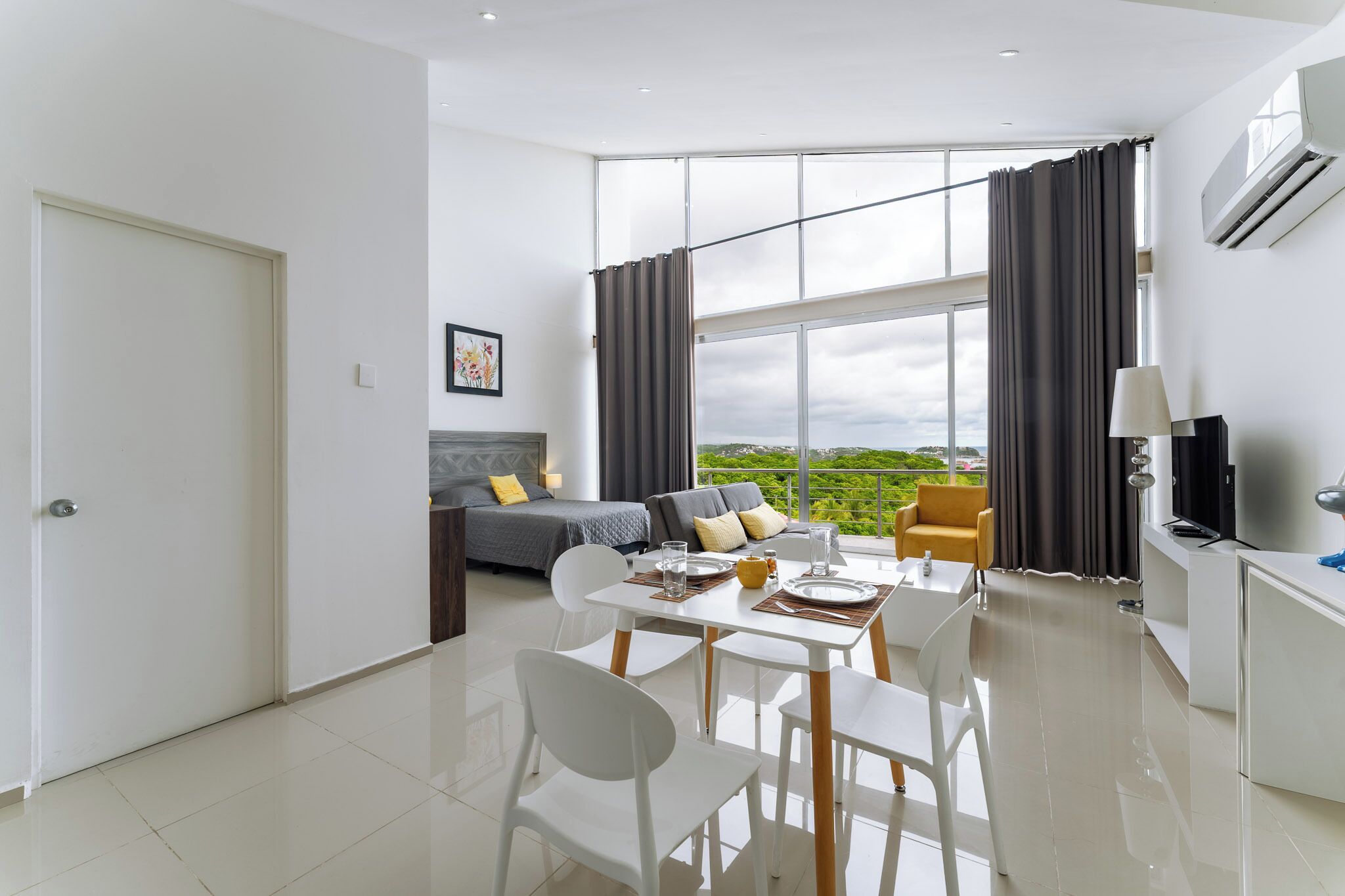 A modern living room with a sofa, a dining table with chairs, a TV, and a large window with curtains.