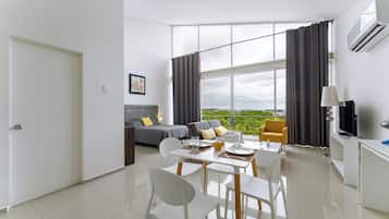A modern living room with a sofa, a dining table with chairs, a TV, and a large window with curtains.