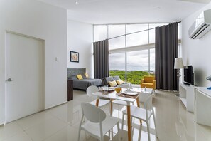 A modern living room with a sofa, a dining table with chairs, a TV, and a large window with curtains.