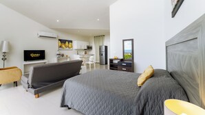 Quarto moderno com cama grande, televisão e cozinha compacta ao fundo.