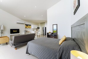 Ein modernes Schlafzimmer mit einem großen Bett, einem Fernseher und einer Küchenzeile im Hintergrund.