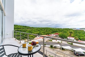 Ein Balkon mit Tisch und Stühlen, einem Geländer und Blick auf eine grüne Landschaft mit Gebäuden in der Ferne.