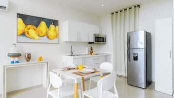A modern kitchen with white cabinets, a stainless steel refrigerator, a microwave, and a dining area with white chairs and a table.