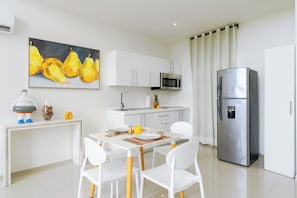 A modern kitchen with white cabinets, a stainless steel refrigerator, a microwave, and a dining area with white chairs and a table.