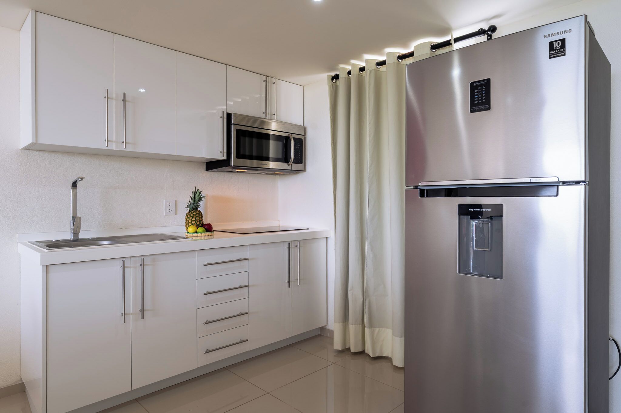 A modern kitchen with white cabinets, a stainless steel refrigerator, a microwave, and a water dispenser.