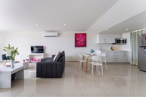 Ein modernes Wohnzimmer mit einer Couch und einem Fernseher, ein Essbereich mit Stühlen und einem Tisch sowie eine Küche mit Schränken und Geräten.