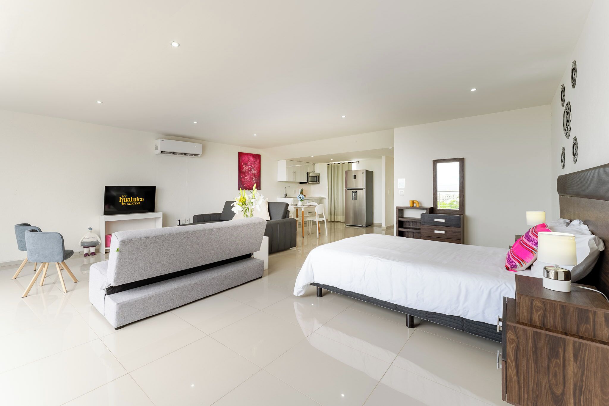 A modern hotel room with a bed, a sofa, a desk, and a kitchenette.