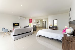 A modern hotel room with a bed, a sofa, a desk, and a kitchenette.