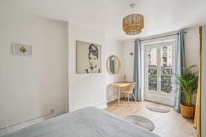 Ein Schlafzimmer mit einem Bett, einem Schreibtisch, einem Stuhl, einer Pendelleuchte, einem Spiegel und einem Fenster mit Vorhängen.