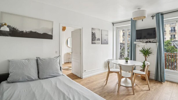 A modern bedroom with a bed, a dining area with a table and chairs, and a balcony with a TV. - Bel Appartement 10 Minutes Pied de la Tour Eiffel (Paris)
