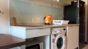 A compact kitchen with a washing machine, a microwave, and a refrigerator. - The Astra Luxe Suite-B604
Prime Location in Central Chiang Mai 
Cozy & Modern (Chang Wat Chiang Mai)
