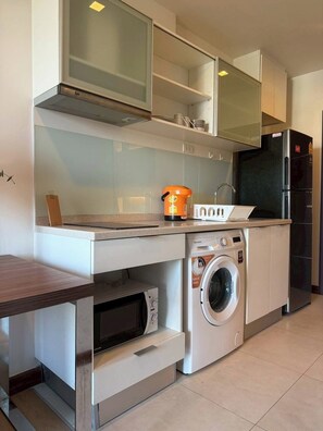 Eine kleine Küche mit Waschmaschine, Mikrowelle und Kühlschrank.