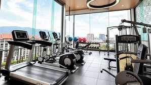 A modern gym with a variety of exercise equipment, large windows offering a city view, and a unique ceiling design. - The Astra Luxe Suite-B604
Prime Location in Central Chiang Mai 
Cozy & Modern (Chang Wat Chiang Mai)