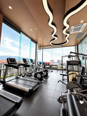 Ein modernes Fitnessstudio mit vielfältigen Trainingsgeräten, großen Fenstern mit Blick auf die Stadt und einem außergewöhnlichen Deckenkonzept.