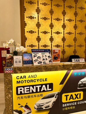A car and motorcycle rental counter with a yellow sign, a taxi service sign, and a decorative wall with a geometric pattern. - The Astra Luxe Suite-B604
Prime Location in Central Chiang Mai 
Cozy & Modern (Chang Wat Chiang Mai)