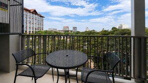 A balcony with two chairs and a table, overlooking a cityscape with buildings and greenery. - The Astra Luxe Suite-B604
Prime Location in Central Chiang Mai 
Cozy & Modern (Chang Wat Chiang Mai)