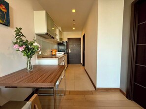 Un estrecho pasillo con una mesa de madera y un jarrón de flores a la izquierda, que conduce a una zona de cocina con un refrigerador y armarios.