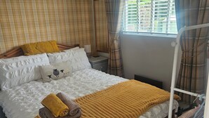 A bedroom with a bed, a bedside table, a mirror, a window with curtains, and a clothing rack. - Cabin Sleeps 4 With Indoor Pool (Tywyn)