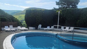 A swimming pool with a tiled edge, surrounded by white lounge chairs and a hedge. - Cabin Sleeps 4 With Indoor Pool (Tywyn)