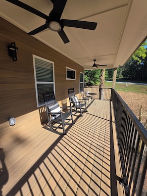 Une terrasse extérieure couverte, dotée d’un ventilateur de plafond, d’un plancher en bois et de deux fauteuils à bascule.