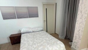 Un dormitorio con cama, mesita de noche, una puerta y vistas al exterior.