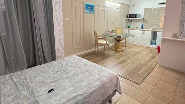 Una habitación pequeña con cama, una mesita, una silla y un kitchenette.