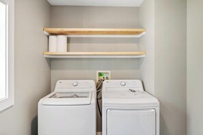 A laundry room with two white washing machines, wooden shelves above, and a power outlet. - *NEW RENTAL* Newly renovated cottage near ski resorts & bike trail! (Petoskey)