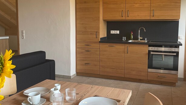 A modern kitchen with wooden cabinets, a black countertop, and a built-in oven. - Bavasol – Your Temporary Bavarian Retreat (Schechen)