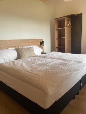 Een slaapkamer met een groot bed, een houten hoofdeinde, een nachtkastje met een lamp en een houten kledingkast.