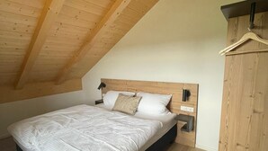 A bedroom with a sloped ceiling, a bed with white bedding, a wooden headboard, a bedside table, and a hanging light fixture. - Bavasol – Your Temporary Bavarian Retreat (Schechen)